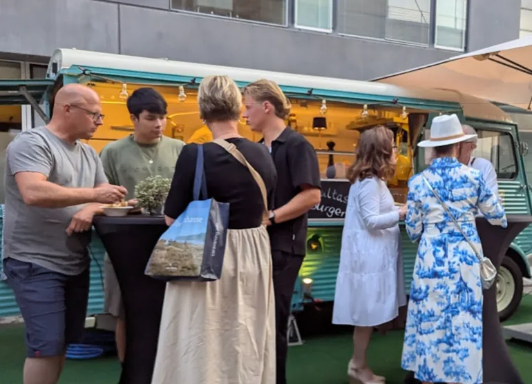Gäste am Stehtisch bei einem Abend-Event vor dem beleuchteten Foodtruck