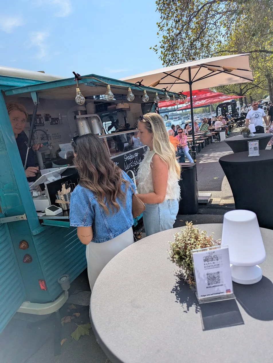 Gäste bestellen am Foodtruck an einem sonnigen Tag am Rheinufer